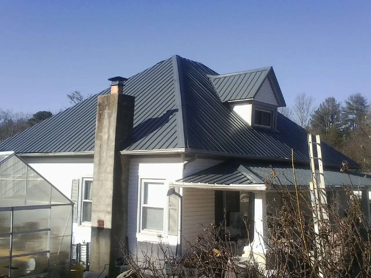 Dark blue standing seam metal roof on a white farmhouse with dormer — Slate & Tile Roof Repair by Roofing Brothers in Greencreek
