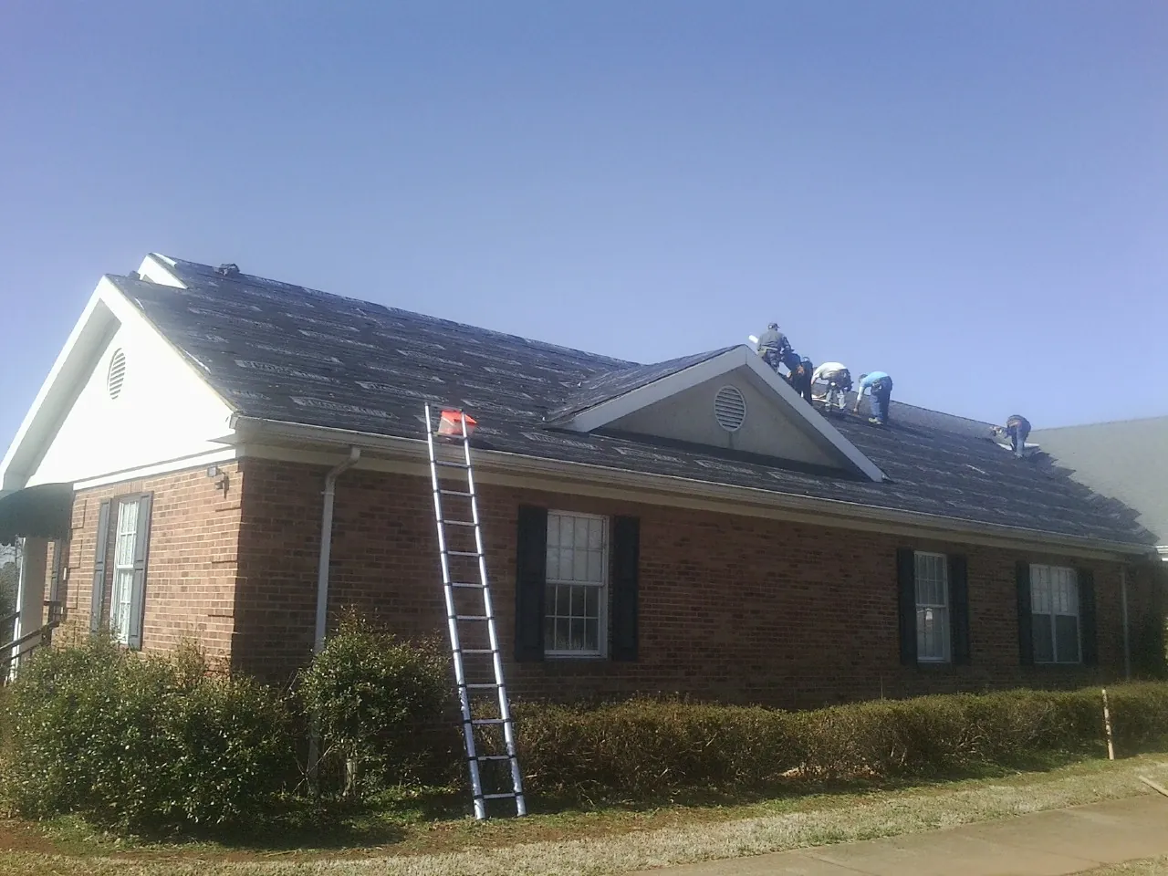 Crew tearing shingles off a brick ranch roof with a ladder set — Metal Roof Repair work by our crew in Greencreek