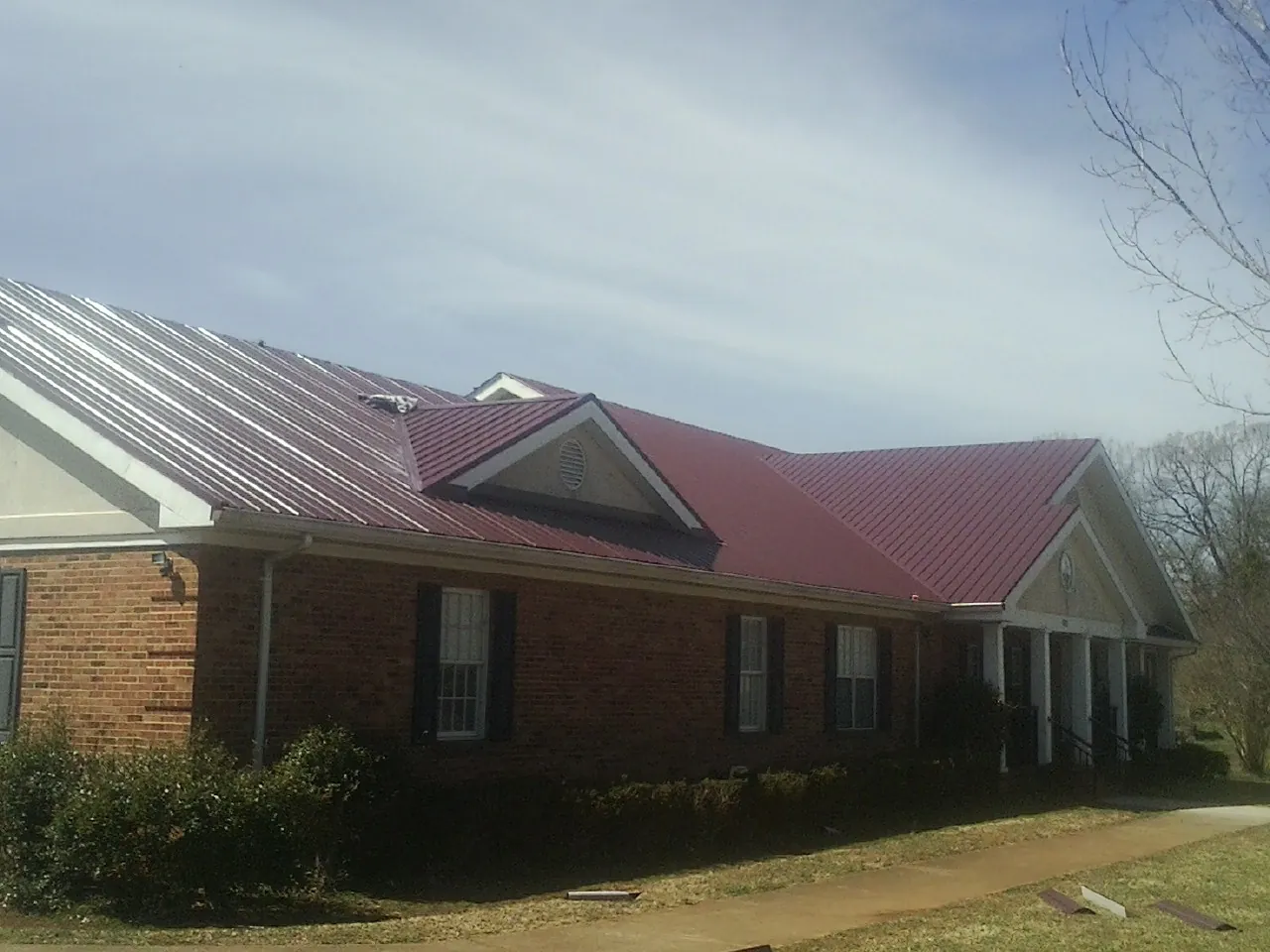 Red metal roof with gabled entries on a long brick building, from a Hail Damage Roof Repair job in Greencreek