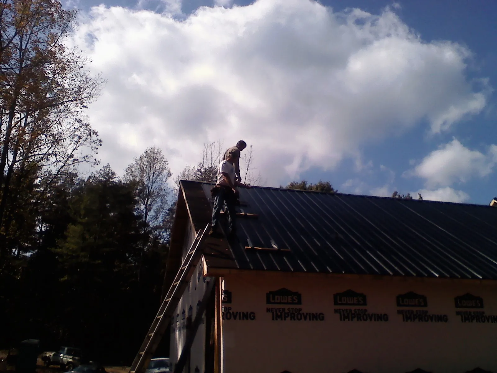 Roofer fastening dark metal panels high against a cloudy sky, from a Roof Inspection job in Greencreek