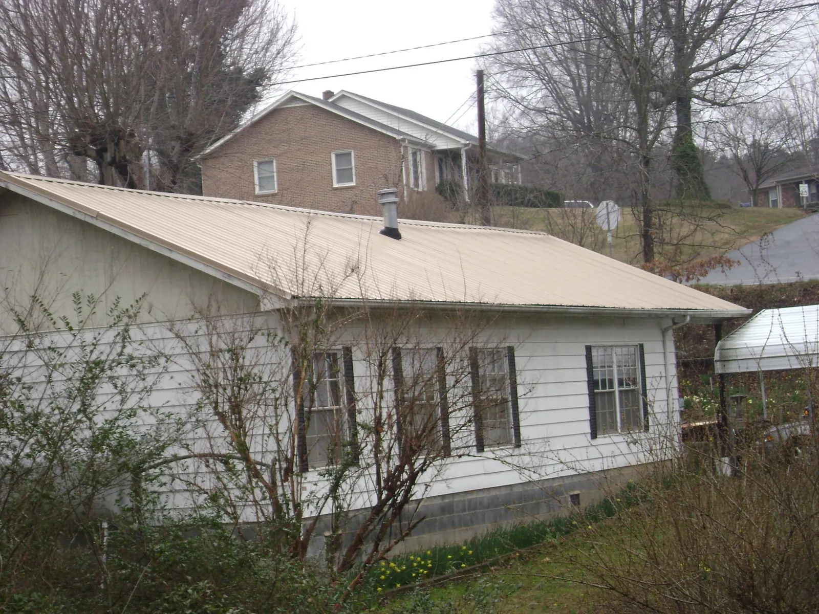 Tan metal roof on a white sided house set into a hillside — Commercial Roofing by Roofing Brothers in Greencreek